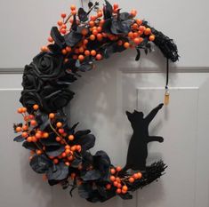 a black cat sitting on top of a wreath with berries and leaves hanging from it