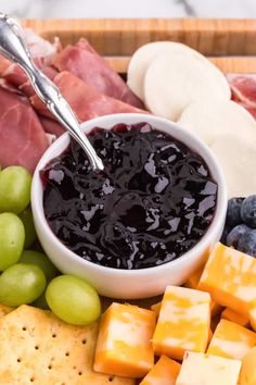 a platter with grapes, cheese, crackers, and meats on it