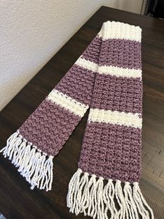 a purple and white crocheted scarf sitting on top of a wooden table next to a wall