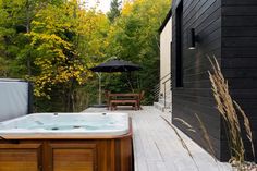 a hot tub sitting on top of a wooden deck next to a black building with trees in the background