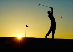 the silhouette of a man playing golf at sunset