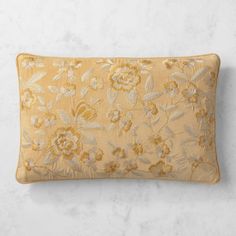 an embroidered pillow on a marble surface with flowers and leaves in the center, along with a white background