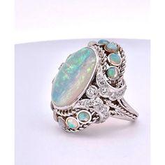 This is part of Chairish’s Fine Jewelry assortment.  This Opal Ring is huge it measures 35mm x 30mm and has beautiful matrix of Blue, Pink, and Yellow.  This cocktail ring has an Opal of 19.82 x 14.82 x 12.90 deep and weighs in at 20.19 grams. It also has 12 smaller Opals of the same color around the center bottom and sides. These Opals are about 0.40 carats each.  This ring is fully chased and detailed underneath.  This ring is sizable but comes in at 6.75 size.  Diamonds surround these stones Opal Diamond Ring, Pink And Yellow, Opal Ring, Opal Rings, Cocktail Ring, Cocktail Rings, Matrix, Diamond Ring, Opal