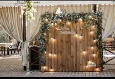 a wooden wall decorated with greenery and fairy lights for a wedding or event venue