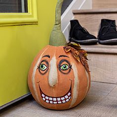 a pumpkin with a face painted on it sitting in front of a yellow door and black shoes