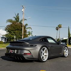 a grey sports car parked in a parking lot next to some palm trees and buildings