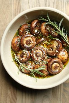 a white bowl filled with sliced mushrooms and rosemary sprinkled on top of it