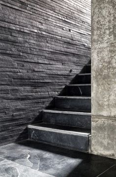 the stairs are made of concrete and have black tiles on each one side, along with stone steps that lead up to an upper level