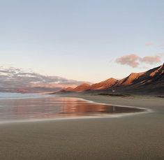 a beach with mountains in the background and water on the sand at sunset or sunrise