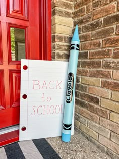 a back to school sign next to a red door with a blue crayon pen