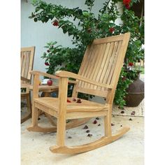 two wooden rocking chairs sitting next to each other in front of a bush with red flowers