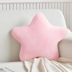 a pink star shaped pillow sitting on top of a white couch next to a blanket