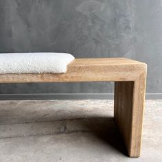 a wooden bench with a white towel on it's back end, in front of a gray wall