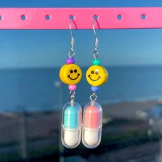 When we made these odd happy pill earrings we didn't hold back - they're weird & quirky and so blooming cute. Which is exactly where we want to be in life  They're fast becoming one of our best sellers and we're so chuffed that you love them just as much as we do! They're also super lightweight so don't worry about them stretching your ears or being too heavy to wear. Forget the boring earrings that everyone else is wearing because these are sure to get everyone's attention. IN A GOOD WAY. Designed & handmade by us, here are some more of the details: - FREE UK DELIVERY - super lightweight  - 2 inch drop  - Silver or gold plated hocks - random colorful glass beads - mismatched cute happy pill charms - adorable clay bright yellow clay charms MADE BY US PICKLES TO MAKE YOU SMILE 😊  WORLDWIDE Strange Earrings, Unique Earrings Weird, Weird Earrings Aesthetic, Maximalist Earrings, Pill Earrings, Odd Earrings, Weird Accessories, Silly Earrings, Earrings Weird