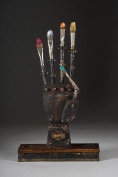 a metal sculpture with five brushes in it's hand and four other tools sticking out of the handle