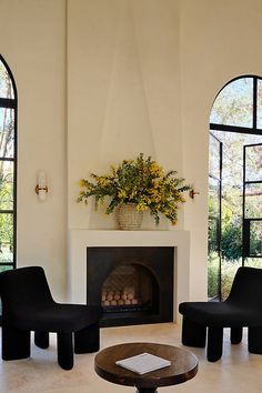 a living room with two black chairs and a fire place in front of an arched window