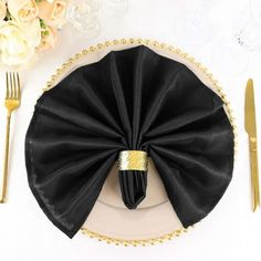 a table setting with black napkins and gold place settings