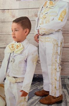 two young boys dressed in white and gold outfits, standing next to each other with their hands on their hips