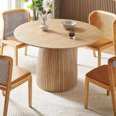 a round wooden table with four chairs around it and a vase on the table top