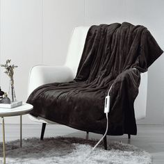 a white chair with a black blanket on top of it next to a coffee table