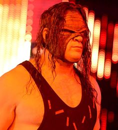 the wrestler is posing for a photo in his wrestling gear, with red and yellow lights behind him