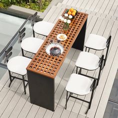 an outdoor dining table with white chairs and plates on it, next to a pool