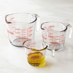 three measuring cups filled with liquid on top of a white counter next to an orange measuring cup