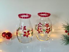 two glass vases decorated with red and white flowers are sitting next to christmas decorations