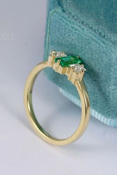 an emerald and diamond ring sitting on top of a blue velvet bag