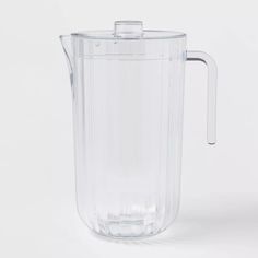 a clear plastic pitcher with a handle on the side and no lid is shown in front of a white background