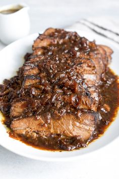 a white plate topped with meat covered in gravy next to a cup of coffee