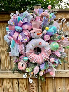 a wreath made to look like a snowman is hanging on a wooden fence outside