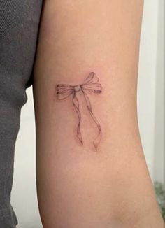 a woman's arm with a small bow tattoo on the back of her left arm