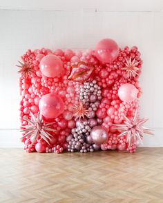 an art work made out of balloons and other items on a wooden floor in front of a white wall