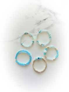 Blue Evil Eye protective Ring Set Chose your size US size 4-13  5 stretchy beaded rings.  Rings are made of a stretchy material with iridescent blue, light blue , and gold  premium glass seed beads plus one tiny evil eye protective bead , one light blue glass bead , and a cube white glass bead.  Handmade,  Perfect summer accessories ! Custom sizes available . Adjustable Light Blue Jewelry With Spacer Beads, Blue Stackable Jewelry With Round Beads, Dainty Blue Beaded Round Bracelets, Dainty Blue Round Beaded Bracelets, Dainty Blue Beaded Bracelets, Trendy Inelastic Round Beaded Jewelry, Light Blue Adjustable Dainty Jewelry, Minimalist Blue Adjustable Stackable Rings, Minimalist Adjustable Blue Stackable Rings