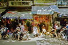 a group of people on motorcycles and scooters in front of shops with awnings