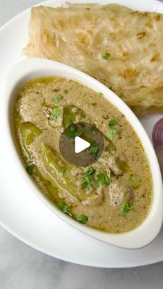 a white plate topped with a bowl of soup next to a slice of bread and onion wedges