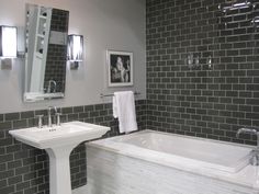 a white bath tub sitting next to two sinks in a bathroom with gray tiles on the walls