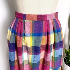 Dash the blues away with a cheerful plaid skirt in shades of magenta, yellow, royal blue, white and green from Eccobay. Side button with straight waistband with pleats in front and elastic waist with gathers in back. Two pockets. Imagine this with a black turtleneck. NOTE: Pinned to fit dress form. Material / 30% wool, 40% polyester, 25% acrylic and 5% other Care / dry clean For accurate fit, please compare measurements to a similar garment that fits you well. Make allowance for clothes undernea Fall Multicolor Skirt With Elastic Waistband, Multicolor Skirt With Elastic Waistband For Fall, 1970s Preppy, Shades Of Magenta, Black Turtleneck, The Blues, Plaid Skirt, Fit Dress, Dress Form