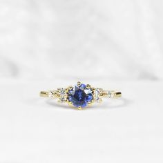 a yellow gold ring with a blue sapphire and three white diamonds on the side, sitting on a white surface