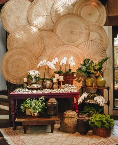 an arrangement of flowers and plants on a table in front of wicker wall art