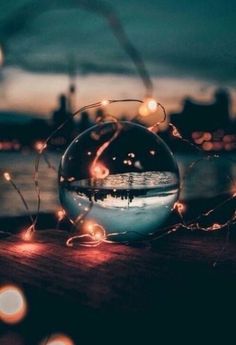 a glass ball sitting on top of a wooden table next to water and lights in the background