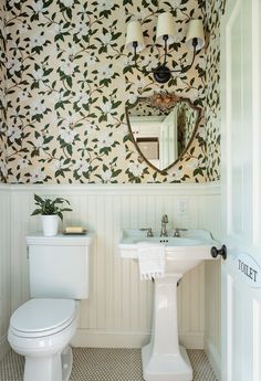 a white toilet sitting next to a sink in a bathroom under a mirror and light fixture