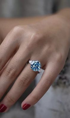 a woman's hand wearing a ring with an oval blue and white diamond on it