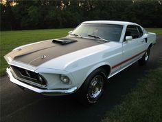 an old mustang is parked on the side of the road in front of some trees