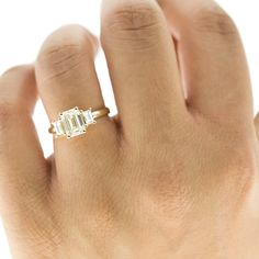 a woman's hand with a diamond ring on top of her left hand and an emerald stone in the middle