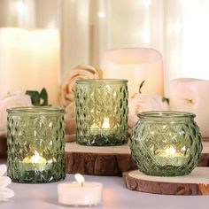 three green glass candle holders sitting on top of a wooden table next to candles and flowers