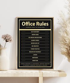 a black and gold office rules poster hanging on a wall next to a potted plant