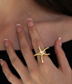 Starfish Ring: ▪️  This gorgeous statement piece will make the perfect gift for yourself or a loved one. The ring is adjustable and will fit different finger sizes   ▪️  Made of gold plated brass   ▪️  The model in the picture is a size 7     Care Instructions:   ▪️  Gold plating can last for years if looked after correctly   ▪️  Keep away from water, sweat, chemicals, perfumes, lotions, etc. If it begins to tarnish in areas of high friction, the color will appear a darker orange   ▪️  How to clean: dip a cotton ball in a solution of mild dish soap and water. Rub gently and then rinse, dry, and buff     We hope you enjoy! We have family ties with jewelers in Istanbul, Turkey who hand make our pieces with love. Your happiness is our utmost priority, and we accept returns if it doesn't meet Hellenic Aesthetic, Jewelry Summer, Statement Ring, خواتم خطوبة, Starfish Ring, Beach Rings, Summer Beach Jewelry, Fantasy Earrings, Summer Rings