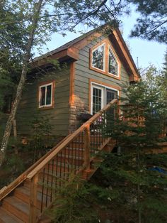 a small cabin in the woods with stairs leading up to it's second floor